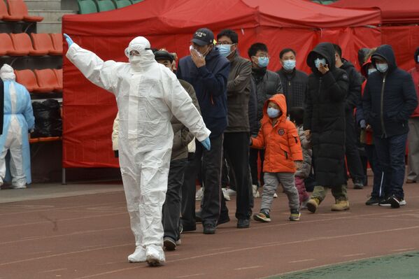 Работник в защитном костюме ведет жителей во временный центр тестирования на коронавирус Covid-19 в Тяньцзине, Китай - Sputnik Латвия