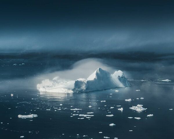 Aisbergi izpeld no miglas kā gigantiskas baltas pilis pie Grenlandes rietumu piekrastes. Laiva kreisajā pusē no ledus kalna dāvā priekšstatu par tā izmēriem - Sputnik Latvija