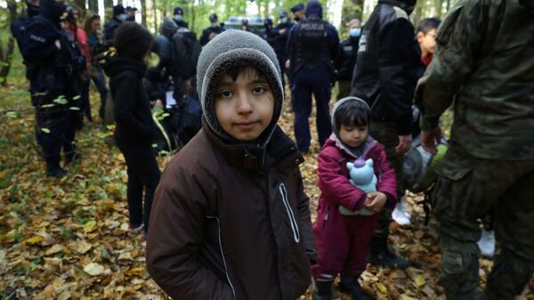 Иракский ребенок в окружении пограничников и полицейских после пересечения белорусско-польской границы в городе Хайнувка, Польша - Sputnik Latvija