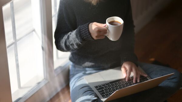 Женщина пьет кофе во время работы за ноутбуком - Sputnik Latvija