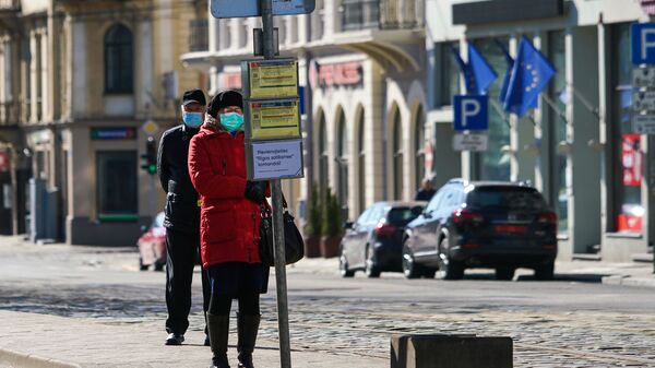 Женщина и мужчина в защитных масках на остановке общественного транспорта в Риге - Sputnik Латвия